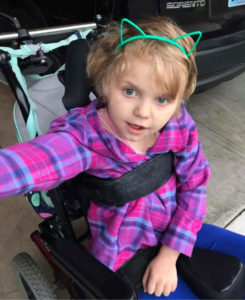 A little girl in a wheelchair wearing green cat ears on her head.