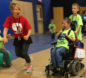 A woman running beside a little boy who is being pushed in his wheelchair by another little boy.