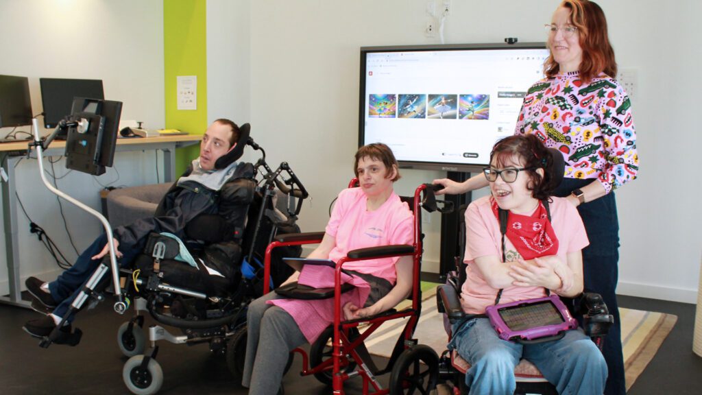 A group of AAC users pose with an SLP in front of a large screen.